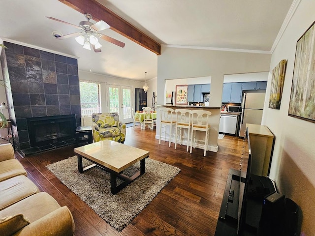living area featuring a tiled fireplace, vaulted ceiling with beams, ornamental molding, dark wood-style flooring, and a ceiling fan
