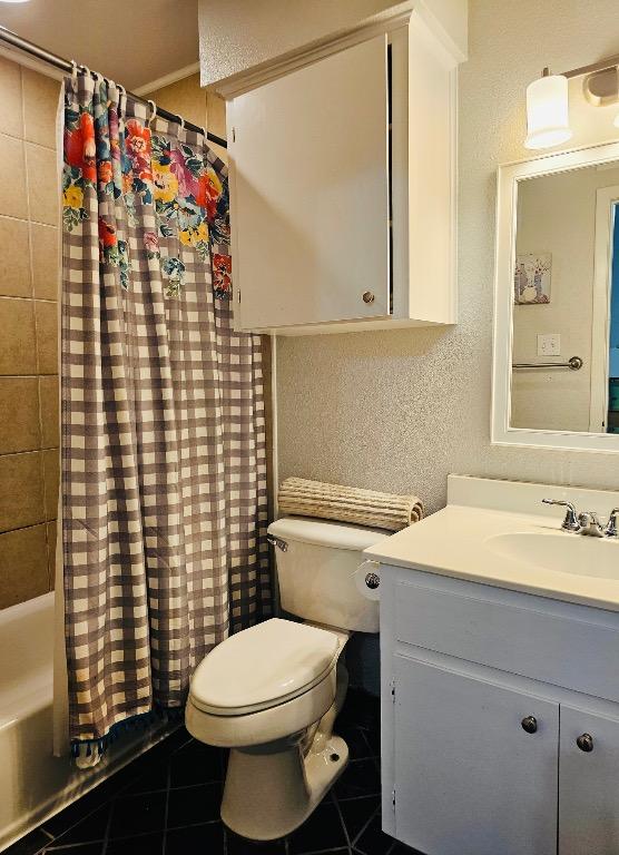 bathroom featuring vanity, a textured wall, toilet, and tile patterned flooring