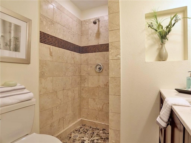 bathroom featuring toilet, a tile shower, and vanity