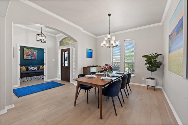 dining area featuring a chandelier, baseboards, arched walkways, ornamental molding, and light wood finished floors