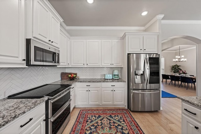 kitchen featuring white cabinetry, stainless steel appliances, crown molding, and arched walkways