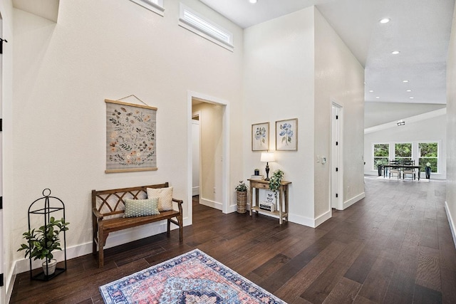 corridor featuring baseboards, recessed lighting, hardwood / wood-style flooring, and a high ceiling