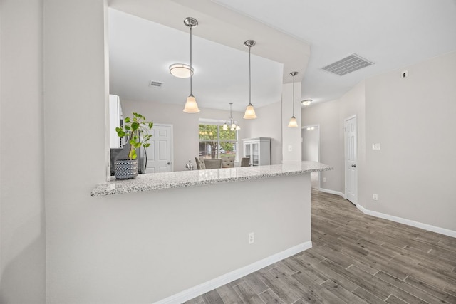 kitchen featuring an inviting chandelier, visible vents, a peninsula, baseboards, and wood finished floors