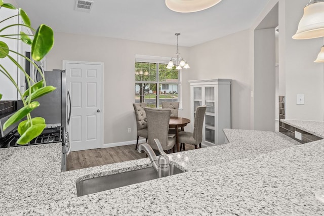 kitchen featuring a sink, visible vents, an inviting chandelier, wood finished floors, and hanging light fixtures