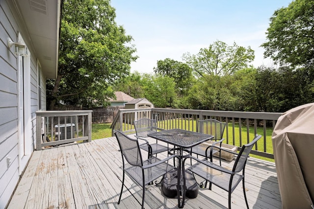 wooden deck featuring outdoor dining space, a storage unit, a yard, and a fenced backyard