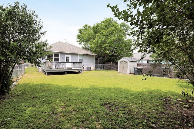 view of yard featuring a storage unit, a fenced backyard, a wooden deck, and an outbuilding