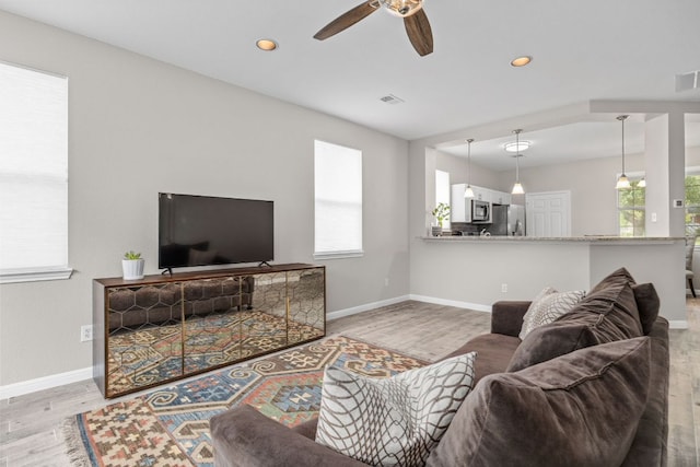 living area featuring baseboards, visible vents, wood finished floors, and a ceiling fan