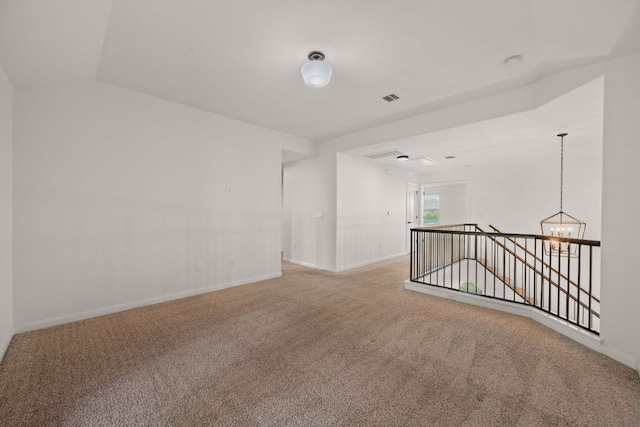 spare room featuring carpet floors, visible vents, baseboards, and a chandelier