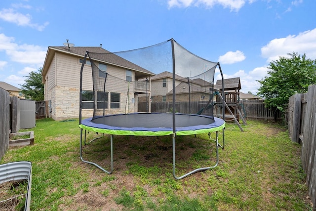 back of property with a lawn, a fenced backyard, a trampoline, and stone siding