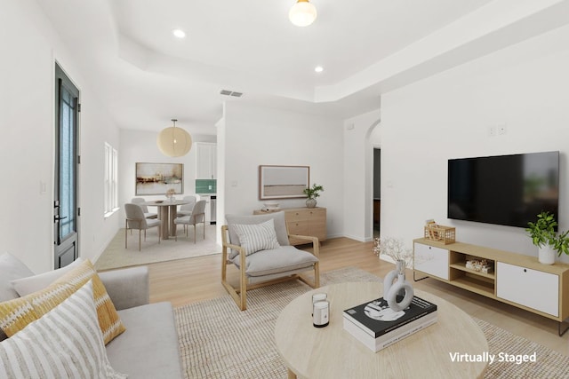 living area featuring visible vents, arched walkways, wood finished floors, and a tray ceiling