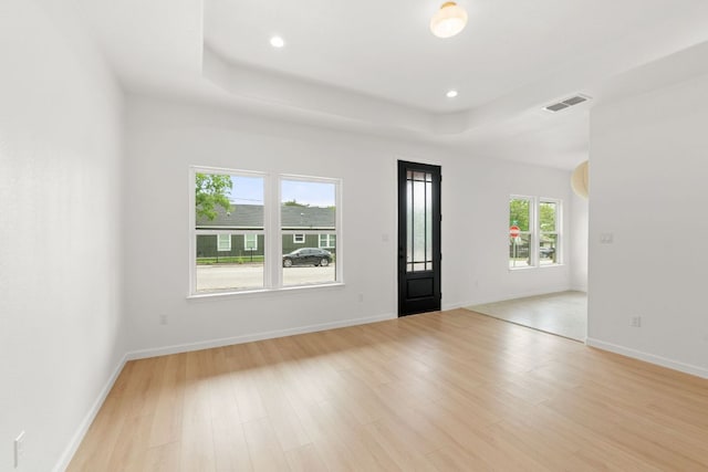 empty room featuring baseboards, visible vents, light wood-style floors, and a tray ceiling