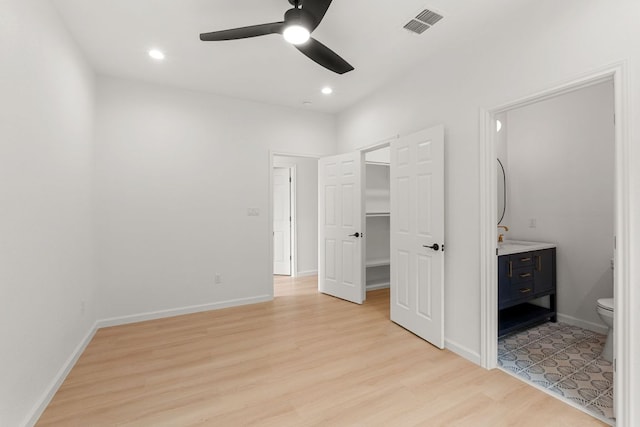 unfurnished bedroom with baseboards, light wood-style flooring, ensuite bathroom, a walk in closet, and visible vents