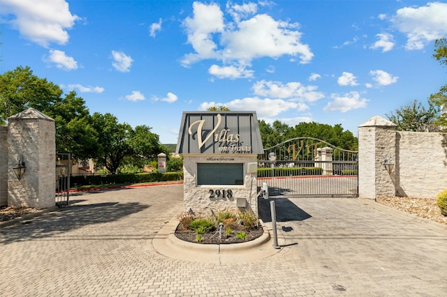 community / neighborhood sign featuring a gate, fence, and curved driveway