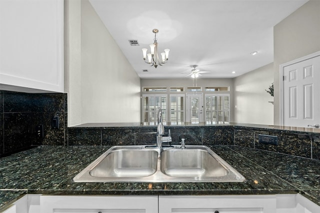 kitchen featuring decorative backsplash, white cabinets, a sink, visible vents, and ceiling fan with notable chandelier