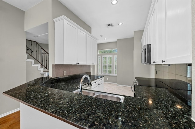 kitchen with stainless steel microwave, a sink, dark stone countertops, visible vents, and baseboards