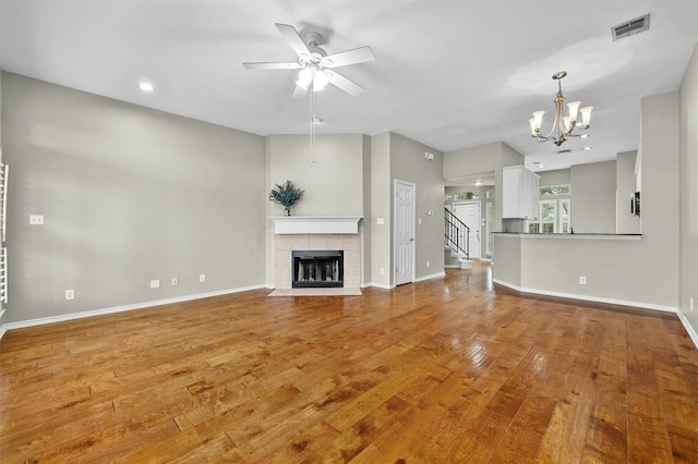 unfurnished living room with visible vents, baseboards, wood finished floors, a tiled fireplace, and ceiling fan with notable chandelier