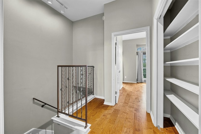hall featuring light wood-style floors, baseboards, and an upstairs landing