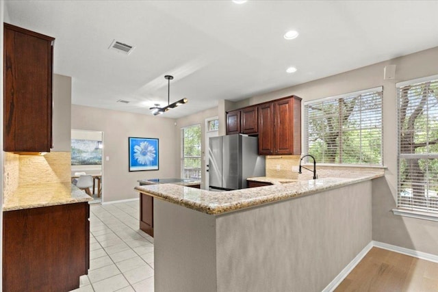 kitchen with visible vents, freestanding refrigerator, light stone countertops, a peninsula, and backsplash