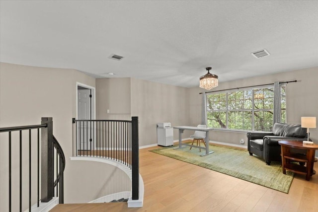living area featuring an upstairs landing, wood finished floors, visible vents, and a notable chandelier