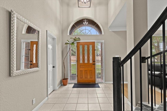 tiled entrance foyer with a textured wall, baseboards, and a high ceiling