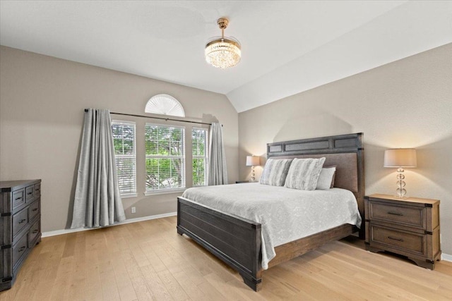 bedroom featuring baseboards, a notable chandelier, lofted ceiling, and light wood-style flooring