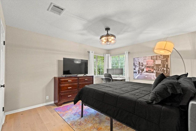 bedroom featuring a textured ceiling, visible vents, baseboards, and light wood-style floors