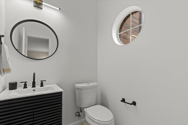 half bath featuring vanity, toilet, and baseboards