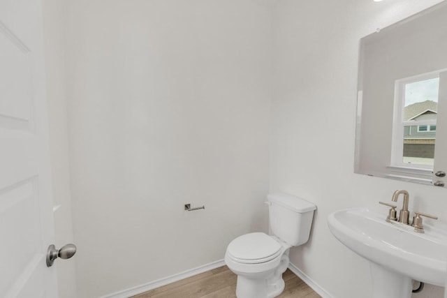 half bathroom with a sink, baseboards, toilet, and wood finished floors