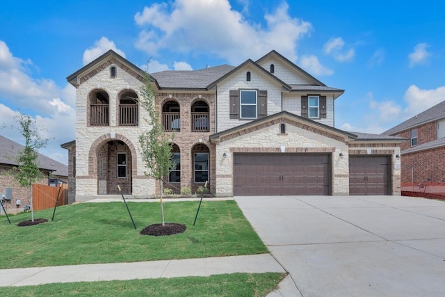 french country home with fence, a front lawn, stone siding, a balcony, and driveway