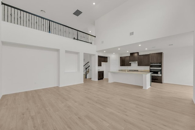 unfurnished living room featuring visible vents, light wood-style floors, a towering ceiling, and stairway