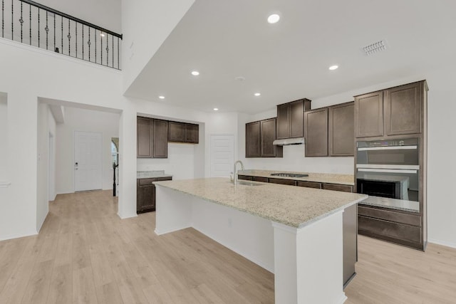 kitchen featuring dark brown cabinetry, appliances with stainless steel finishes, a center island with sink, a sink, and light wood-style floors