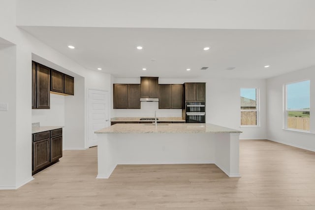 4847 Padula Dr, Round Rock, TX 78665 - kitchen featuring light wood-style floors, dark brown cabinetry, a spacious island, recessed lighting, and light stone counters