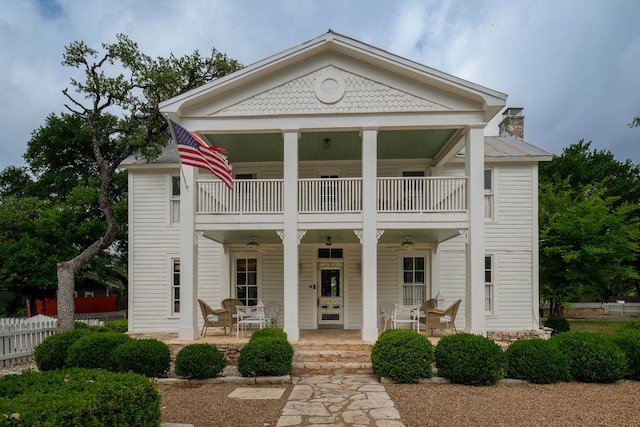 view of front of house with a chimney, a porch, fence, a ceiling fan, and a balcony