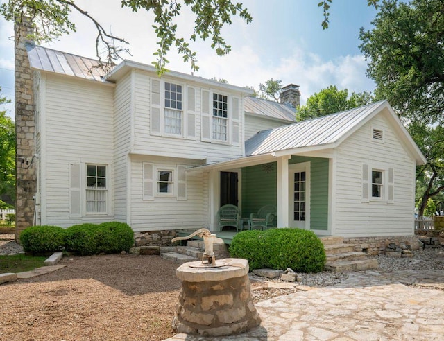 back of property with metal roof, a standing seam roof, a porch, and a chimney