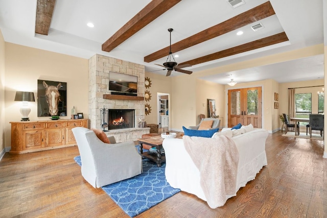 living room with beamed ceiling, visible vents, a fireplace, wood finished floors, and a ceiling fan