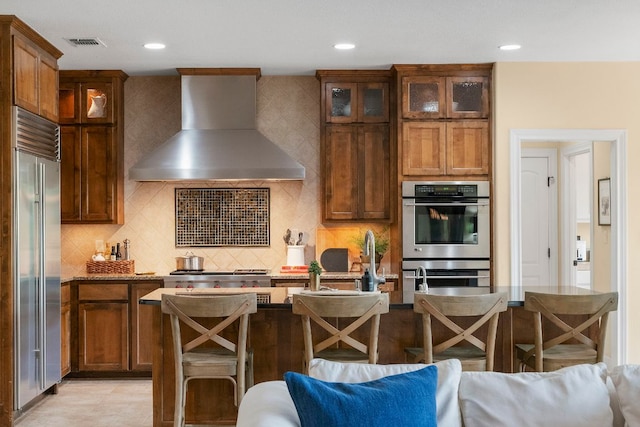 kitchen with glass insert cabinets, stainless steel appliances, recessed lighting, wall chimney exhaust hood, and backsplash