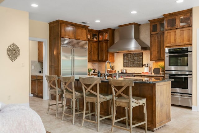 kitchen featuring a warming drawer, wall chimney exhaust hood, visible vents, backsplash, and appliances with stainless steel finishes