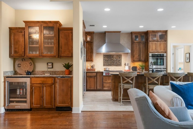 kitchen featuring wall chimney range hood, tasteful backsplash, beverage cooler, recessed lighting, and wood finished floors