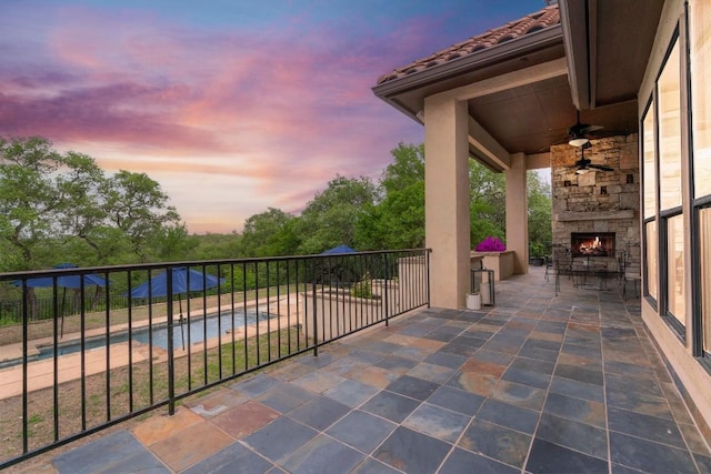 view of patio / terrace featuring a ceiling fan, an outdoor stone fireplace, and a fenced in pool