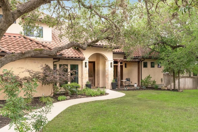 mediterranean / spanish-style home featuring a front yard, stucco siding, a tiled roof, and fence