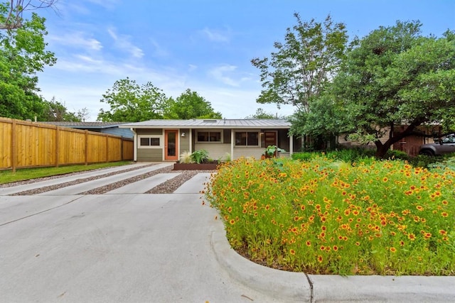 single story home featuring fence, a standing seam roof, concrete driveway, and metal roof