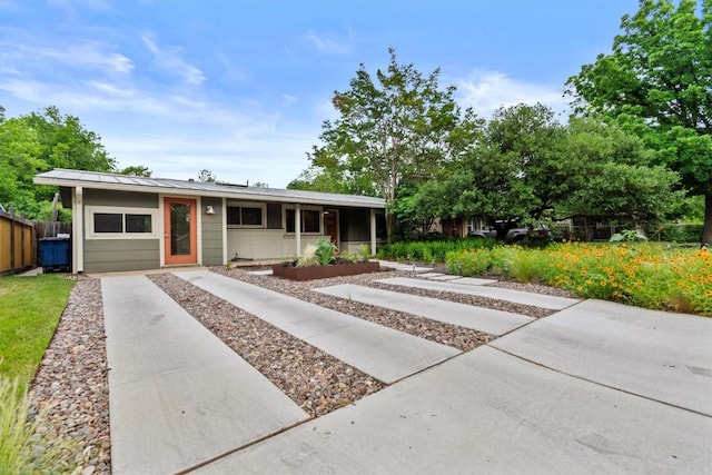 ranch-style house featuring metal roof, a standing seam roof, driveway, and fence