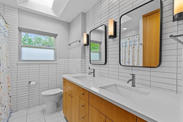 bathroom featuring double vanity, a sink, toilet, and tile walls