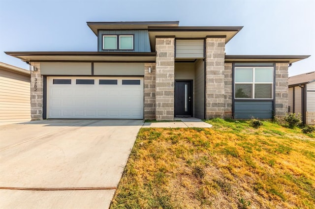 prairie-style home with a front yard, concrete driveway, and stone siding