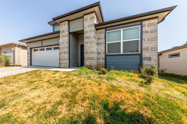 prairie-style house with concrete driveway, stone siding, a front yard, and an attached garage