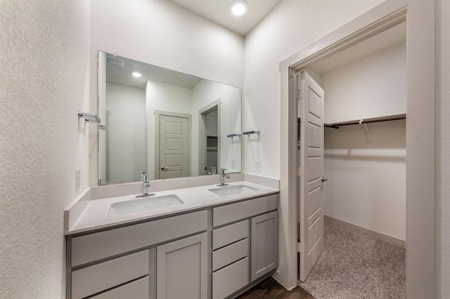 bathroom with a walk in closet, double vanity, a sink, and a textured wall