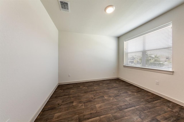 empty room with dark wood-style floors, visible vents, and baseboards