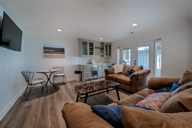 living area with french doors, baseboards, indoor wet bar, beverage cooler, and light wood-style flooring