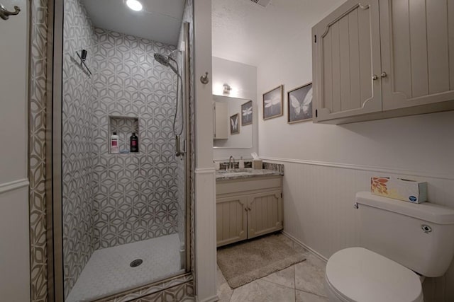 full bath with tile patterned flooring, vanity, toilet, a wainscoted wall, and a stall shower