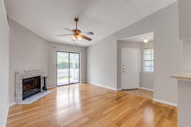 unfurnished living room featuring a tiled fireplace, baseboards, a ceiling fan, and light wood finished floors